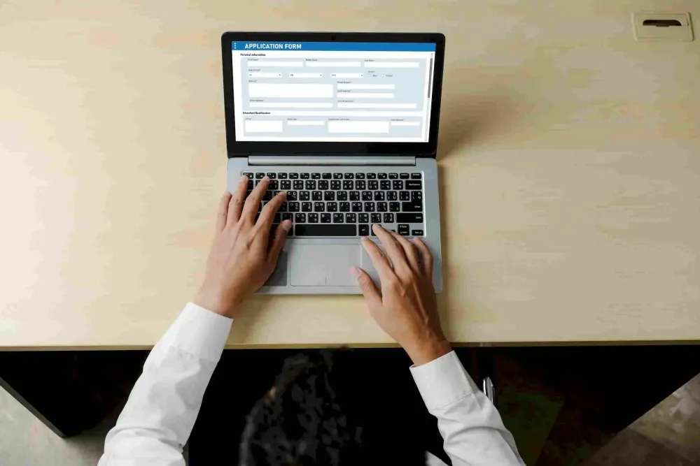 Affordable Apartments with Person filling out an online application form on a laptop at a desk, viewed from above.