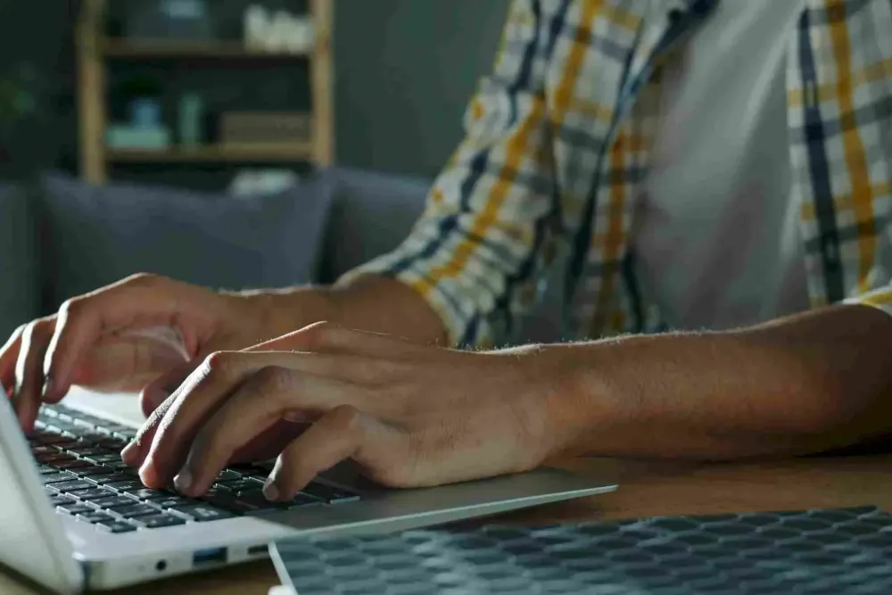Affordable Apartments with Person typing on a laptop at a desk, wearing a plaid shirt, with a blurred background.